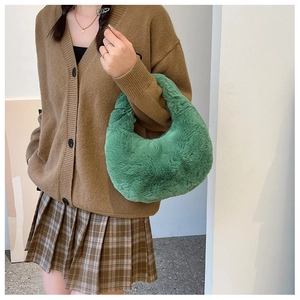 Detail view of the green plush crescent handbag held by a model in casual knitwear