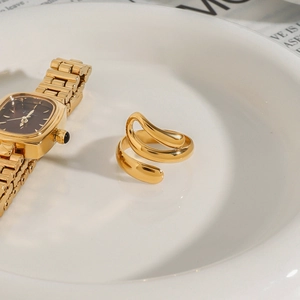 Detail of a gold spiral stainless steel ring on a white plate next to a gold watch