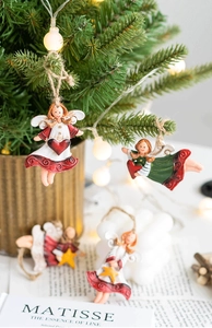 Detail of resin Christmas angel ornaments with red and green skirts on pine branch