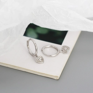 Macro shot of silver heart earrings with textured 3D pendants and elegant hoop closure