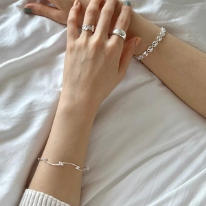 Detail of layered S925 sterling silver bracelets and rings on a soft fabric background