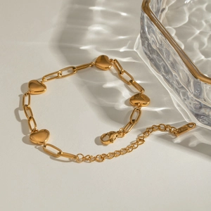 Gold stainless steel paperclip chain bracelet with multiple heart charms on beige background