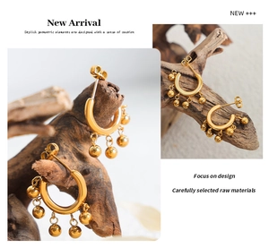Detail of C-shaped gold tassel earrings with five small metal beads on rustic wood