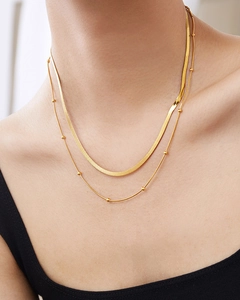 Detailed view of layered gold titanium steel flat snake chain and beaded necklace on neck