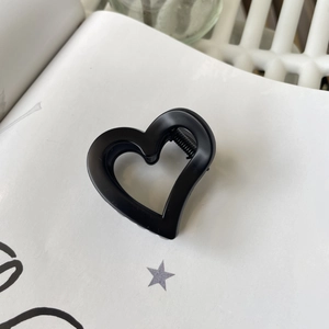 Detail of a black heart-shaped matte hair claw clip placed on a white book page