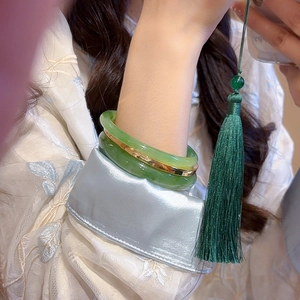 Close-up of double-layered light green jade bracelets with gold metal spacer and dark tassel