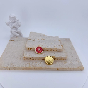 Minimalist gold and red enamel lemon slice pendant on beige textured stone base