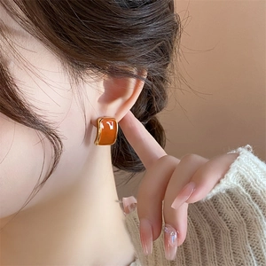 Close-up of a model wearing the square orange enamel earrings with golden metal edges