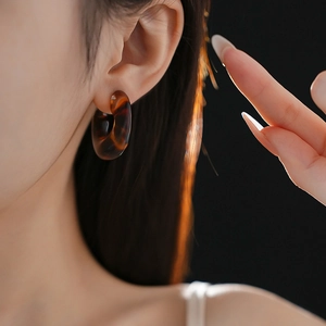 Close-up of leopard print resin C-shaped hoop earrings on model with warm lighting