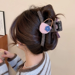 Detail view of a large knitted bow hair claw clip with floral accents on a bun