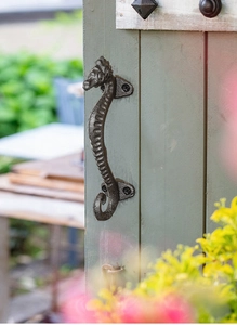 Close-up of vintage seahorse-shaped cast iron handle mounted on a light green wooden door