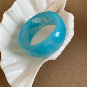Close-up of blue marble resin oval bangle on a white shell tray with high gloss finish