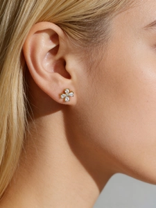 Macro shot of gold floral stud earrings featuring pear-cut clear stones on model