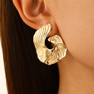 Detailed view of irregular gold fan earrings with spiral texture on a female model