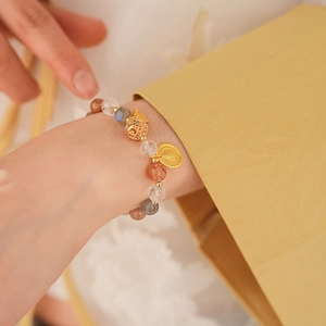 Detail of beaded gemstone bracelet with gold fish charm and coin on a female wrist