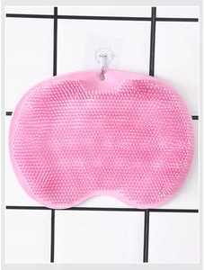 Pink silicone back scrubber mat with dense bristles and hanging hole on white tiled wall