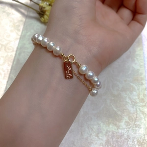 Close-up of Baroque pearl bracelet with 14K gold plated clasp and engraved tag on wrist