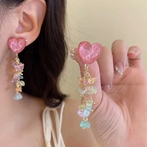 Close-up of pink heart earrings with colorful stone tassels worn on an ear