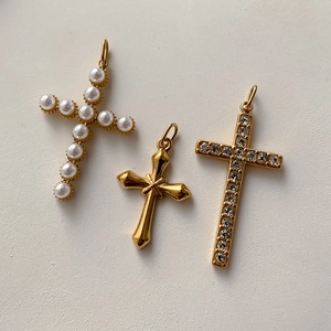 Dettaglio di tre ciondoli a croce con perle, finitura in oro lucido e strass brillanti