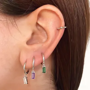 Macro shot of silver geometric earrings with transparent, purple, and green zircon pendants