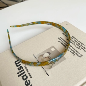 Detail van een smalle acetaat hoofdband met geel en blauw schildpadpatroon op boek