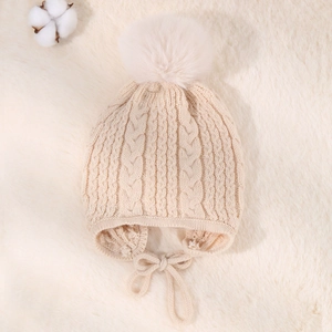 Macro view of beige cable-knit baby earflap hat with soft faux fur pompom and ties