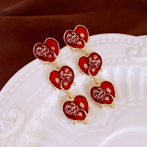 Detailed close-up of triple red heart drop earrings with golden rose embossing