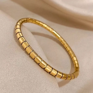 Detailed view of gold Tubogas style flexible bracelet on champagne silk fabric surface