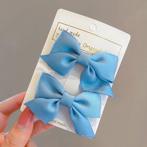 Close-up of two light blue satin bow hair clips displayed on a white handmade card