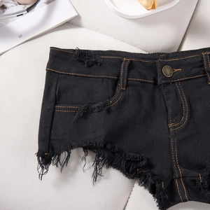 Dettaglio degli shorts in denim nero con cuciture gialle a contrasto e orlo sfilacciato