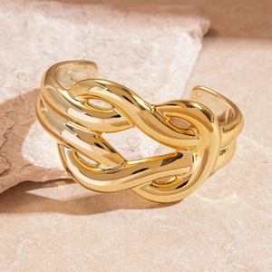 Detail of a polished gold twisted knot bangle on a minimalist stone surface