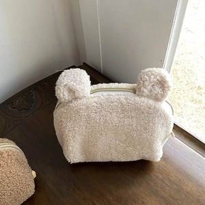 Dettaglio della trousse in peluche beige a forma di orsetto con orecchie e zip dorata