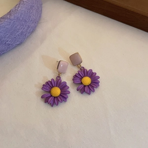 Close-up of purple daisy earrings with yellow centers and gold finish on fabric