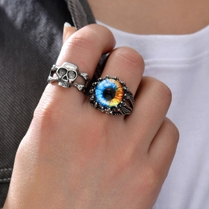 Close-up of gothic silver skull ring and colored evil eye ring set on finger