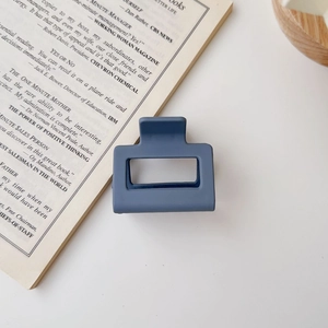 Close-up of a matte blue square hair claw clip placed on an open book with minimalist aesthetic