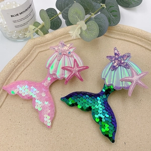 Close-up of sequin mermaid tail and seashell hair clips on a ceramic tray with pearls