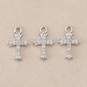 Close-up of three silver baroque cross charms with clear gemstones on beige fabric