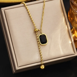 Close-up of a gold-tone necklace with a black rectangular pendant on a beige jewelry box