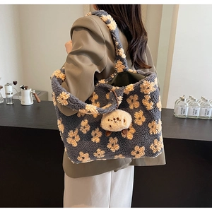 Detail der grau-blauen Plüschtasche mit Blumenmuster und süßem Lamm-Anhänger im Café