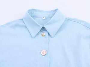 Detailed macro view of light blue linen shirt collar with pearlescent shell buttons
