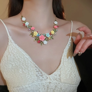 Close-up of floral necklace featuring colorful enamel flowers, green leaves, and pearls