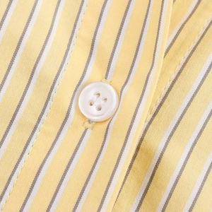 Macro view of yellow and white striped fabric with a stitched white four-hole resin button
