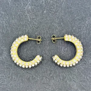 Detailed close-up of C-shaped 18k gold earrings with micro-set rhinestones on stone