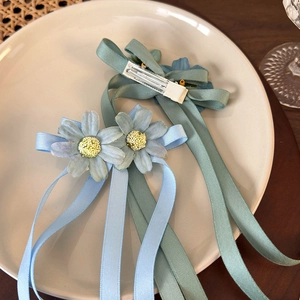 Detailed view of blue and green daisy floral hair clips with ribbons on a ceramic plate