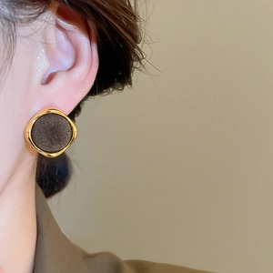Detail of vintage gold-rimmed geometric stud earring with textured dark circular inlay