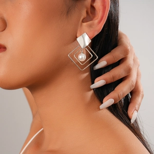 Macro detail of geometric silver diamond earrings with pearl on model