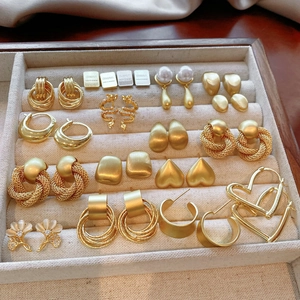 Collection of vintage gold geometric and heart earrings on a soft beige velvet display