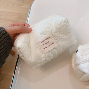 Détail d'une pochette en dentelle matelassée crème avec étiquette brodée et texture en maille