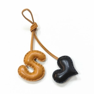 Detail of leather letter S and black heart charm with delicate stitching on bag accessory