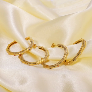 French vintage C-shape gold earrings with multicolored zircon on beige satin fabric